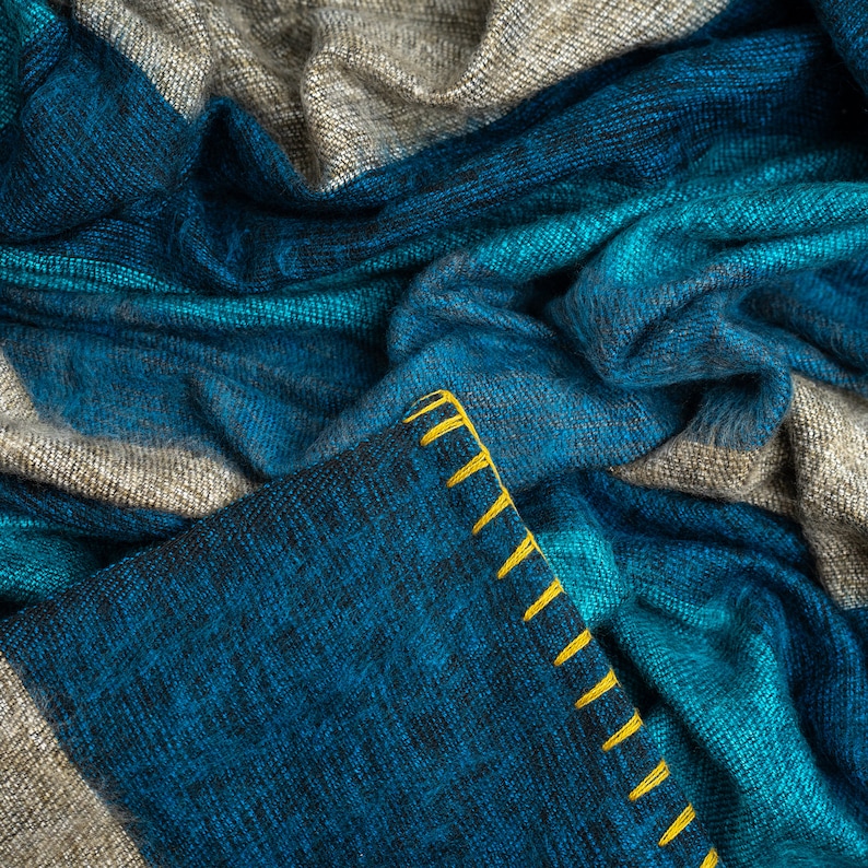 May include: A blue and gray striped throw blanket with a yellow stitched border. The blanket is made of a soft, fuzzy material and is perfect for cuddling up on the couch.