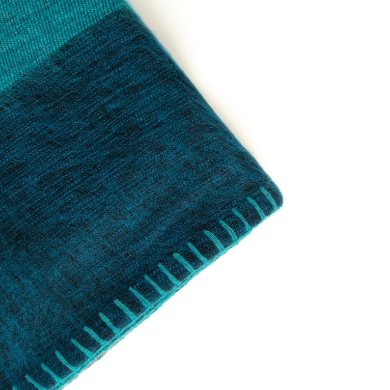 May include: Close-up of a teal blue and dark blue woven blanket with a stitched edge.