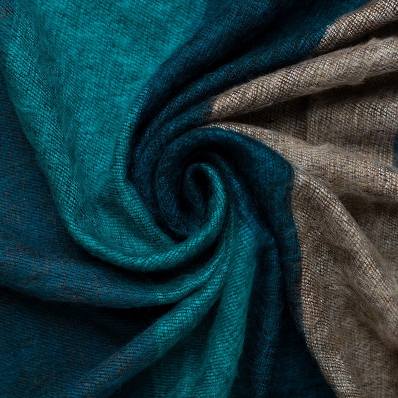 May include: A soft, teal, blue, and brown striped scarf made of woven fabric. The scarf is folded and twisted into a spiral shape.