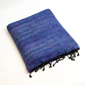 May include: Folded blue and purple scarf with black fringe. The scarf has a textured weave and a mix of blue and purple hues. The fringe is at the bottom edge of the scarf.