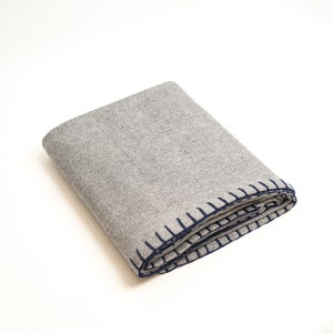 May include: A gray and white herringbone throw blanket with a navy blue stitched border.