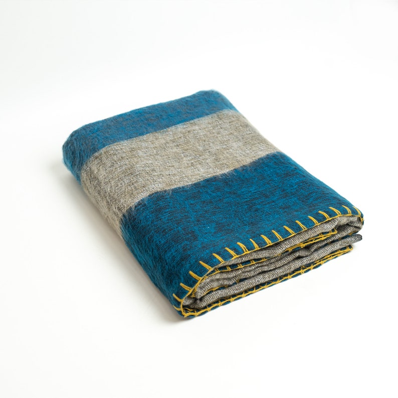 May include: A folded blue and gray striped throw blanket with yellow stitching around the edges.
