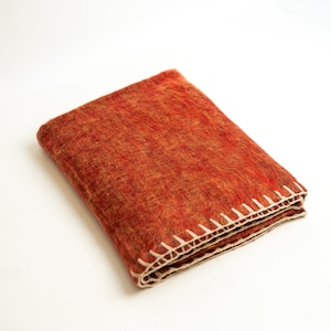 May include: A folded orange throw blanket with a white crocheted trim.