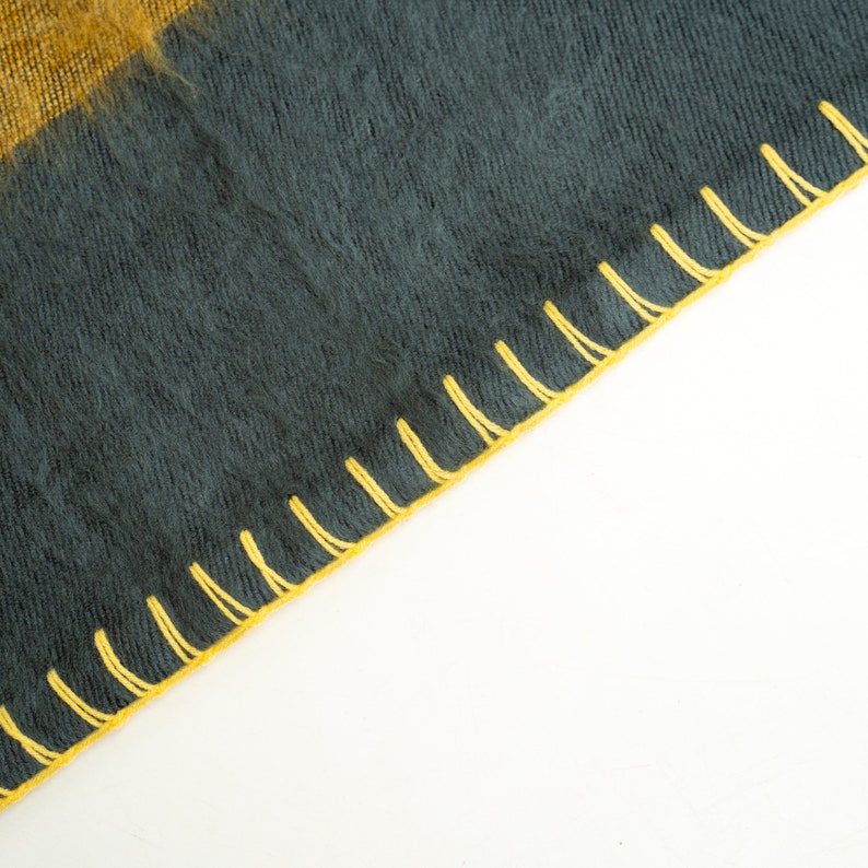 May include: A dark grey fabric with a yellow stitched border. The fabric has a fuzzy texture.