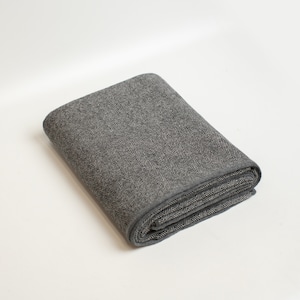 May include: A gray and white herringbone patterned throw blanket folded on a white surface.
