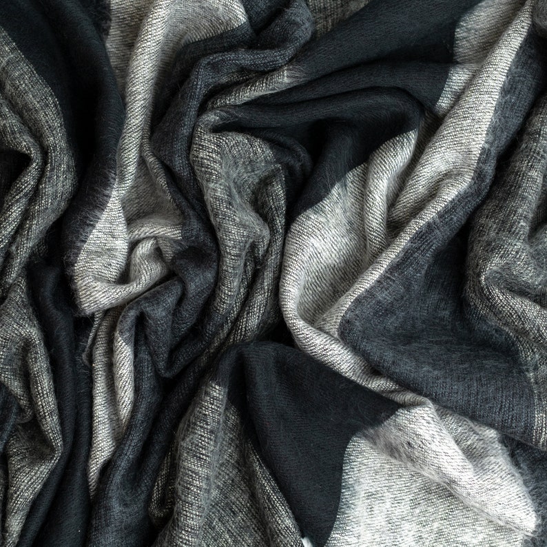 May include: A soft, black and gray plaid blanket with a textured, fuzzy surface. The blanket is folded and draped in a way that shows the texture and pattern.