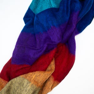May include: A colorful, striped scarf in shades of teal, blue, purple, red, orange, and olive green. The soft, textured fabric is draped against a white background. This accessory is suitable for adding a pop of color to any outfit.