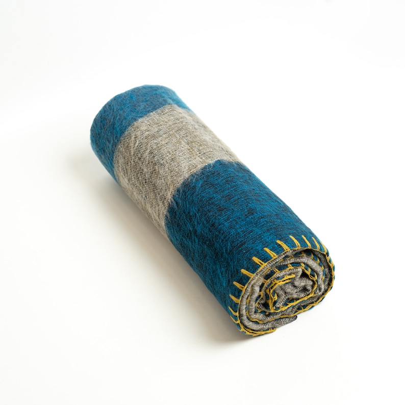 May include: A rolled up blue and gray striped blanket with yellow stitching. The blanket is made of a soft, fuzzy material.