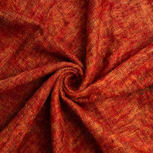 Puede incluir: Primer plano de una tela roja y naranja con un patr&oacute;n tejido texturizado. La tela est&aacute; doblada y retorcida en forma de espiral.
