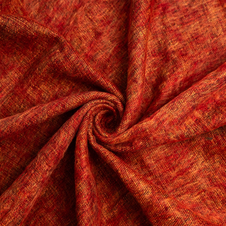 Puede incluir: Primer plano de una tela roja y naranja con un patr&oacute;n tejido texturizado. La tela est&aacute; doblada y retorcida en forma de espiral.