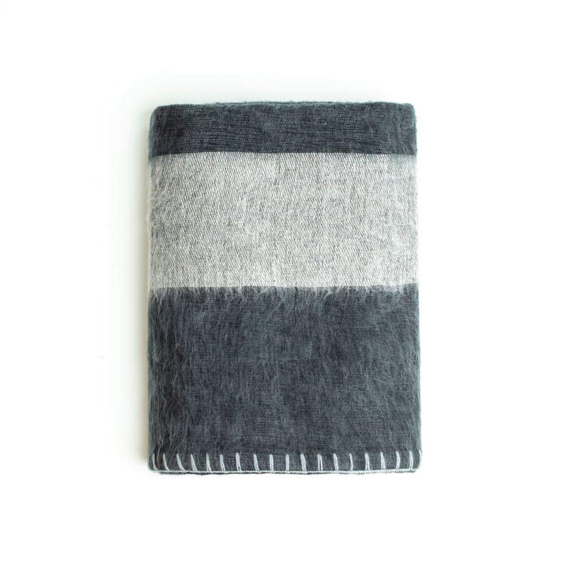 May include: A gray and white striped throw blanket with a fuzzy texture. The blanket is folded and has a white stitched edge.