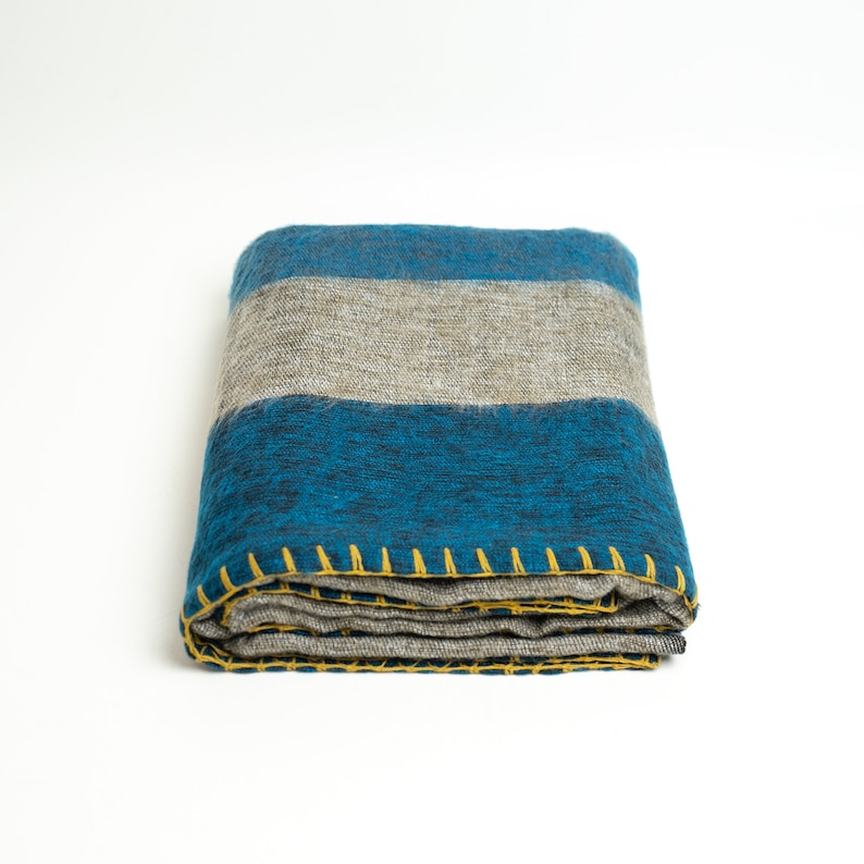 May include: A folded blue and gray striped throw blanket with yellow stitching. The blanket is made of a soft, fuzzy material.