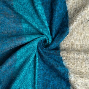 May include: A close-up of a blue and beige fabric with a textured woven pattern. The fabric is folded and twisted, creating a swirling effect.