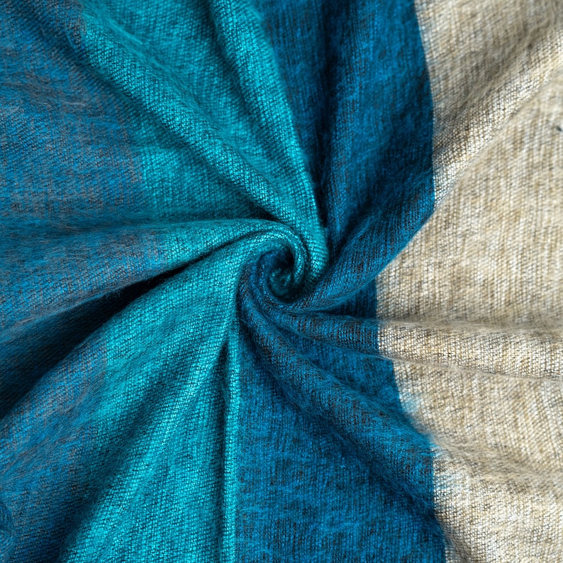 May include: A close-up of a blue and beige fabric with a textured woven pattern. The fabric is folded and twisted, creating a swirling effect.