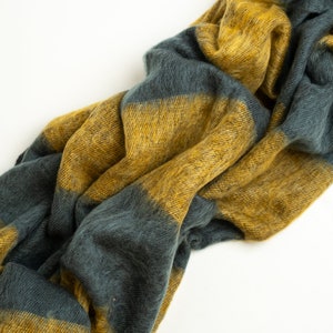 May include: A soft, striped throw blanket in shades of mustard yellow and dark teal. The blanket is made of a fuzzy, textured material and is folded in a loose, casual way.