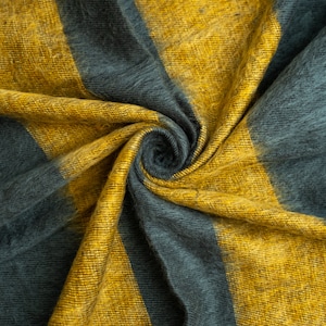 May include: A soft, fuzzy fabric with yellow and grey stripes. The fabric is folded and twisted, creating a swirling pattern.