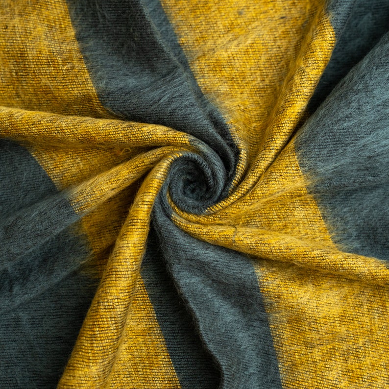 May include: A soft, fuzzy fabric with yellow and grey stripes. The fabric is folded and twisted, creating a swirling pattern.