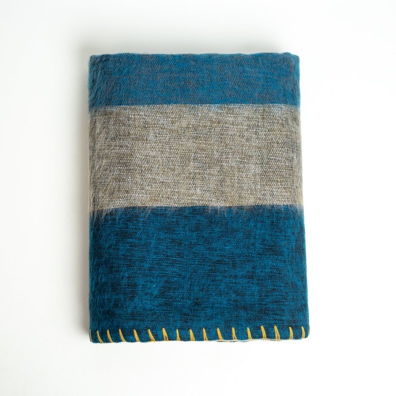 May include: A blue and gray striped throw blanket with a yellow stitched border. The blanket has a textured woven pattern.