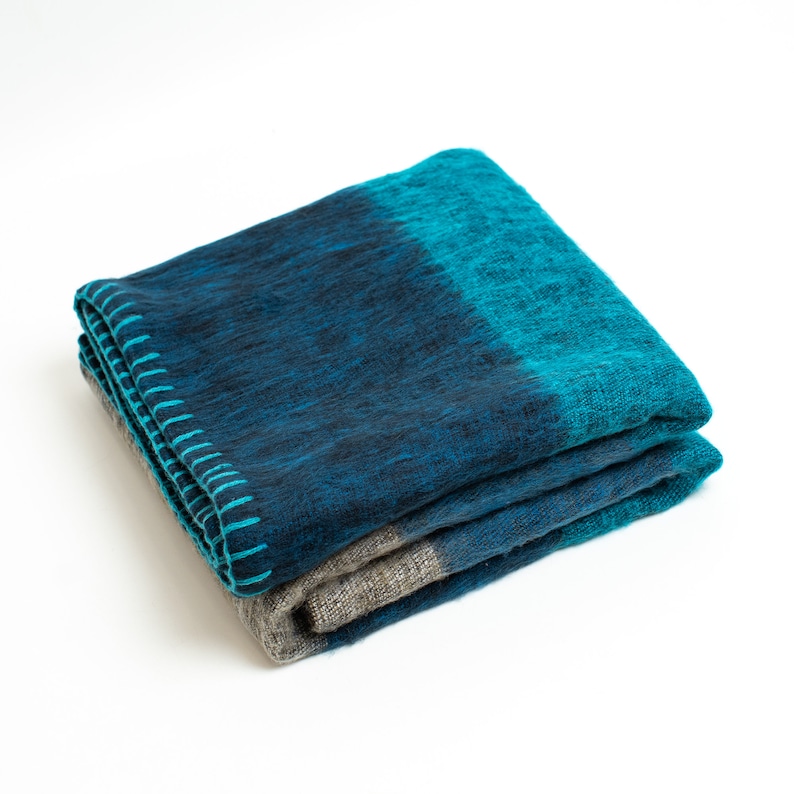 May include: A folded blue and teal throw blanket with a gray underside. The blanket is made of a soft, fuzzy material.