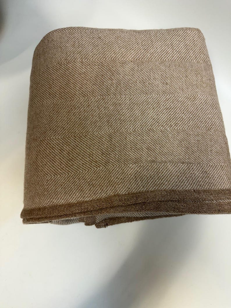 K&ouml;nnte beinhalten: Gefaltete braune und beige Decke mit Fischgr&auml;tenmuster. Die Decke hat ein klassisches Fischgr&auml;tenmuster in einer warmen, neutralen Farbgebung. Die Kanten sind sauber verarbeitet, was auf Qualit&auml;t hindeutet. Ideal f&uuml;r Heimdekoration und Komfort.