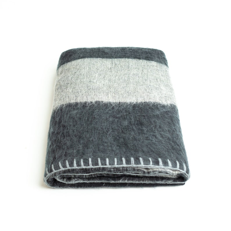 May include: A folded gray and white striped throw blanket with a stitched edge.