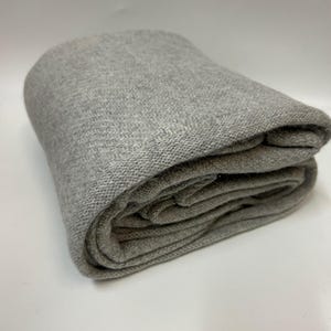 May include: A folded, light gray blanket. The blanket is made of a soft, knitted material. The edges are neatly folded, and the blanket appears to be thick and warm. The background is plain white.