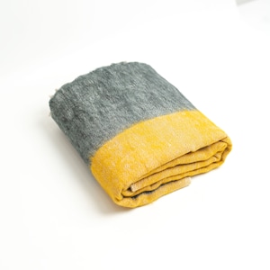 Op de afbeelding: Gevouwen handdoek met grijs en gele strepen. Het bovenste gedeelte is grijs en gaat over in een heldergele streep. De handdoek is netjes opgevouwen en toont de textuur en het kleurcontrast. De handdoek is gemaakt van een zacht materiaal.