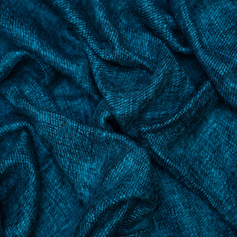 May include: Close-up of a teal fabric with a woven texture. The fabric is draped, creating soft folds and shadows. The color is a deep, rich teal, with subtle variations in tone. The overall appearance suggests a luxurious textile, possibly for clothing or home decor.