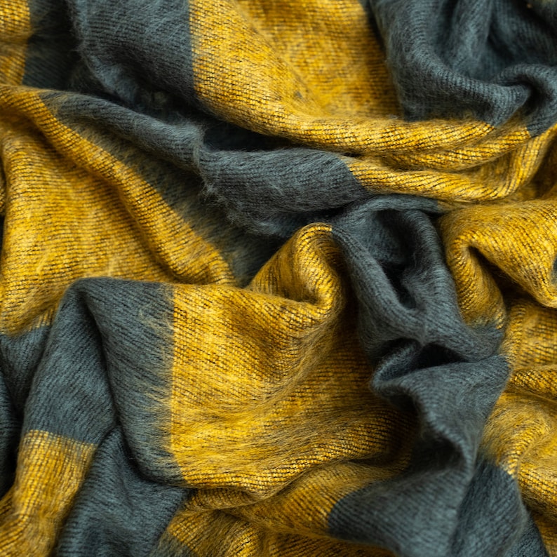 May include: A close-up of a soft, woven fabric with a yellow and dark grey striped pattern. The fabric is textured and has a fuzzy appearance.