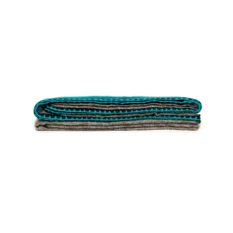 May include: A folded teal and brown striped blanket. The blanket is folded in thirds and has a textured surface.
