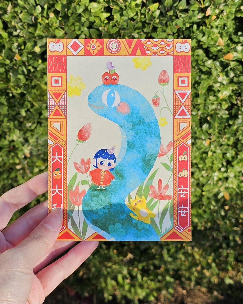 May include: A colorful postcard featuring a whimsical illustration. A blue snake-like creature is the central figure, with a small character in a red outfit. The card has a decorative border with Chinese characters and floral elements.