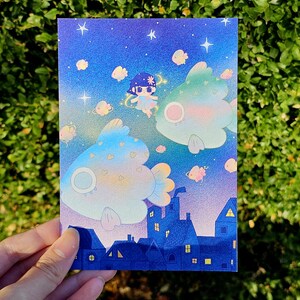 May include: A whimsical illustration featuring a night sky with stars and floating fish. A small figure with a flower crown floats near the fish. Below, a row of blue houses with lit windows adds a touch of fantasy.