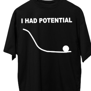 Könnte beinhalten: Schwarzes T-Shirt mit dem weißen Text "I HAD POTENTIAL" über einer weißen Linienzeichnung, die einen Ball zeigt, der eine schräge Ebene hinunterrollt. Das T-Shirt hängt an einem Holzkleiderbügel.