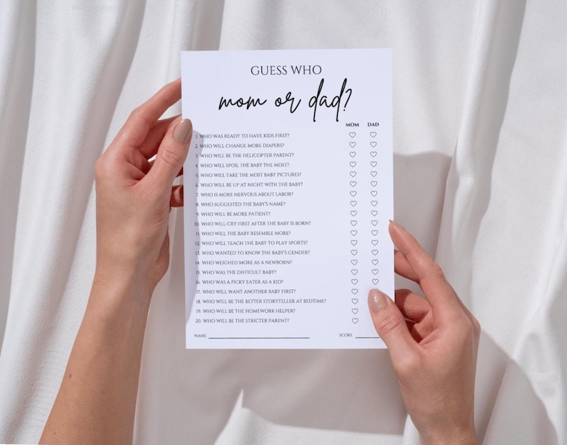 K&ouml;nnte beinhalten: Ein wei&szlig;es Papier-Spielblatt mit dem Text "Guess Who mom or dad?" wird von zwei H&auml;nden gehalten. Das Spielblatt enth&auml;lt eine Liste von Fragen und Felder zum Ankreuzen von Mama oder Papa. Das Spiel ist f&uuml;r eine Babyparty.