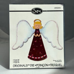 May include: A Sizzix Originals die package, item 655655, featuring an illustration of an angel with yellow hair, a gold halo, and a dark red dress with a floral pattern and white wings. The text reads Angel #2, Originals, and Large.