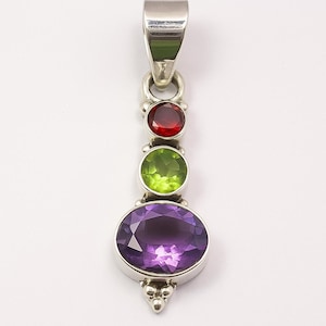 May include: A silver pendant with three gemstones: a red, a green, and a large oval purple stone. The pendant has a decorative silver bail and a cluster of silver beads at the bottom. The gemstones are set in silver.