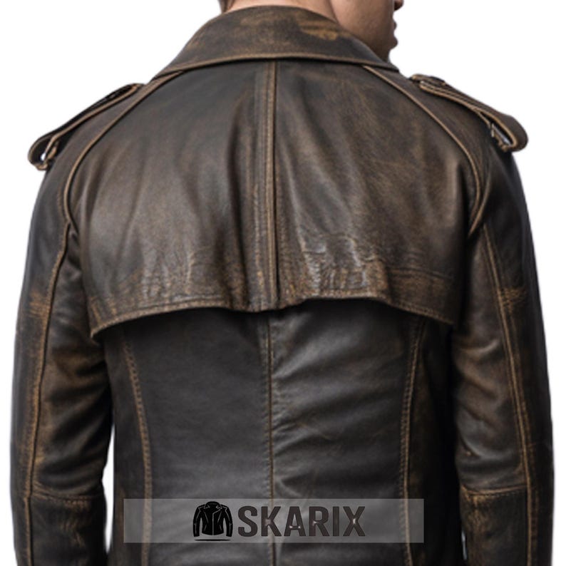 May include: A distressed brown leather jacket with a classic trench coat design. The jacket features a notched collar, shoulder epaulets, and a back cape. The leather has a worn, vintage appearance, with visible texture and color variations. The brand name "SKARIX" is at the bottom.
