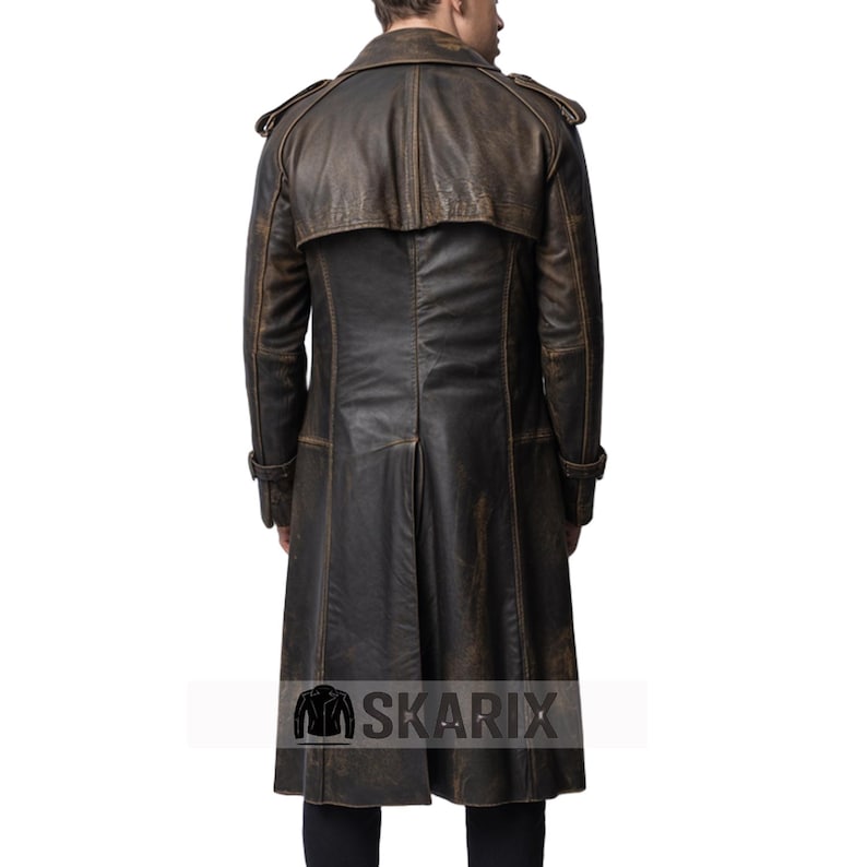 May include: A long, brown leather coat with a distressed finish. The coat features a double-breasted design, epaulettes on the shoulders, and a long, flowing skirt. The back of the coat has a vent at the bottom. The Skarix logo is visible at the bottom.