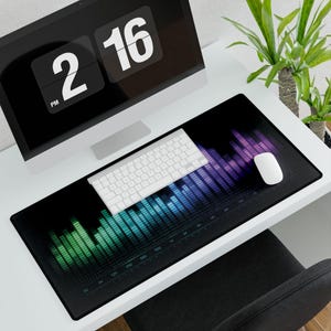 May include: A black rectangular desk mat with a colorful equalizer design, a white keyboard, and a white mouse. A computer monitor displays the time as 2:16 PM. A green plant is in the background.