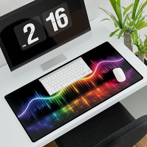 May include: A black rectangular mouse pad with a vibrant, colorful graphic design. The design features a wave of rainbow colors, with a white keyboard and mouse on top. A computer monitor displays the time.