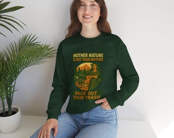 Puede incluir: Sudadera verde oscuro con el texto "MOTHER NATURE IS NOT YOUR MOTHER" y "PACK OUT YOUR TRASH". El gráfico presenta a una mujer con un vestido verde frente a una escena de bosque. La sudadera es de cuello redondo y manga larga.