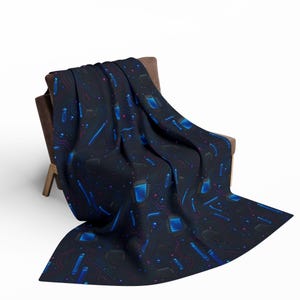 May include: A dark blue throw blanket draped over a brown chair. The blanket features a repeating pattern of blue and purple circuit board designs, including microchips and lines. The blanket is made of a soft material.