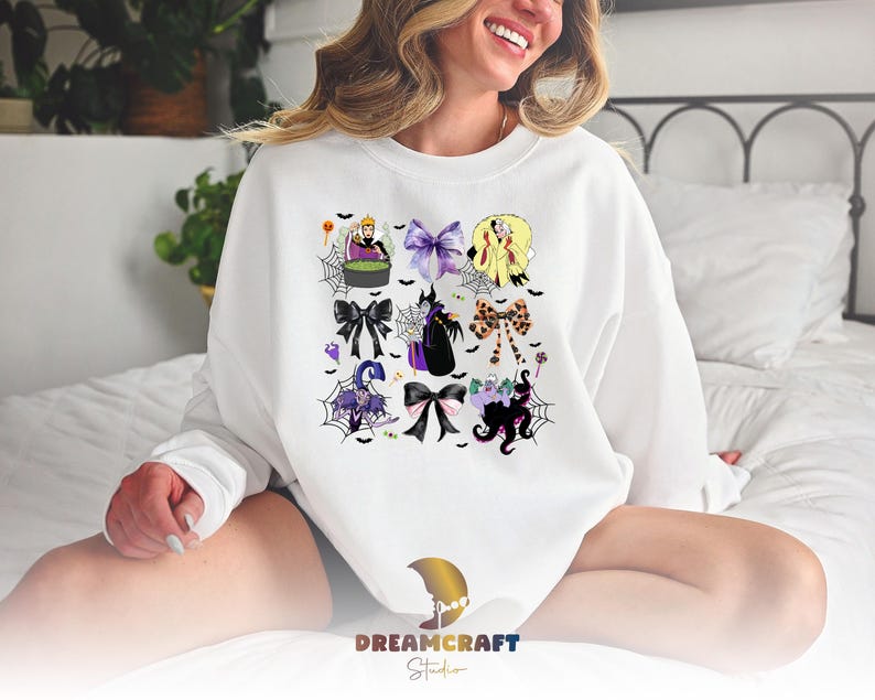 K&ouml;nnte beinhalten: Wei&szlig;es Sweatshirt mit einem farbenfrohen Aufdruck von Halloween-Schleifen und -Figuren. Das Design umfasst lila, schwarze und gelbe Schleifen, Spinnweben und Zeichentrickfiguren. Das Sweatshirt hat lange &Auml;rmel und einen Rundhalsausschnitt.