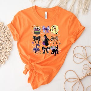 K&ouml;nnte beinhalten: Orangefarbenes T-Shirt mit einem Halloween-Motiv. Das Design zeigt verschiedene Schleifen und Cartoon-B&ouml;sewichte, mit Spinnweben und einem Kessel. Das T-Shirt besteht aus einem weichen Material und hat einen Rundhalsausschnitt.