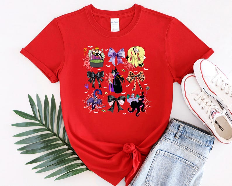 K&ouml;nnte beinhalten: Ein rotes T-Shirt mit einem farbenfrohen Grafikdesign verschiedener Cartoon-Charaktere und Schleifen. Das Design enth&auml;lt Bilder einer Hexe, eines Kessels und Spinnweben. Das Shirt wird mit blauen Jeans und wei&szlig;en Turnschuhen kombiniert.
