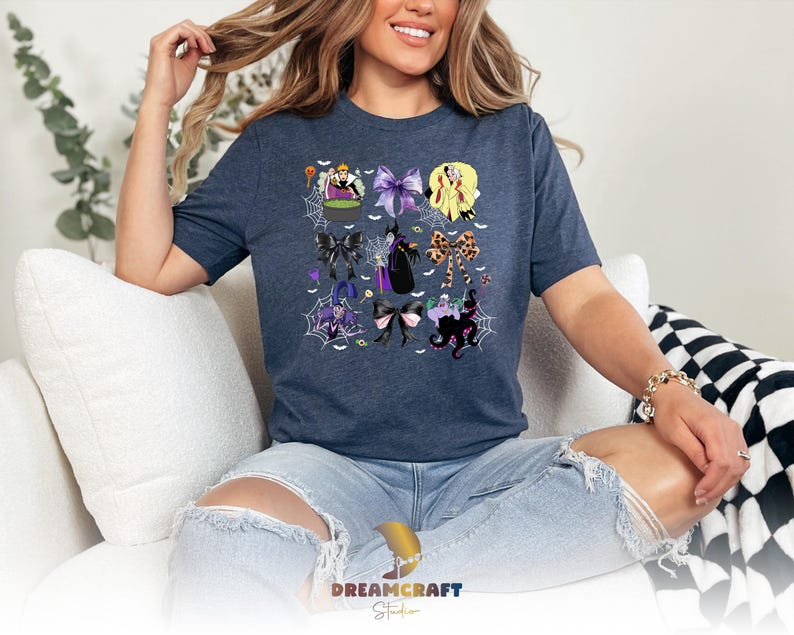 K&ouml;nnte beinhalten: Ein marineblaues T-Shirt mit einem farbenfrohen Grafikdesign von Halloween-Charakteren und Schleifen. Das Design enth&auml;lt Bilder von Hexen, Spinnen und anderen gruseligen Elementen. Der Text "DREAMCRAFT Studio" ist unten sichtbar.