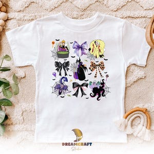 K&ouml;nnte beinhalten: Wei&szlig;es T-Shirt mit einem farbenfrohen Aufdruck von Schleifen und Halloween-Charakteren. Das Design umfasst Schurken, Spinnweben und Flederm&auml;use. Das T-Shirt hat einen Rundhalsausschnitt und kurze &Auml;rmel, f&uuml;r ein Kind.