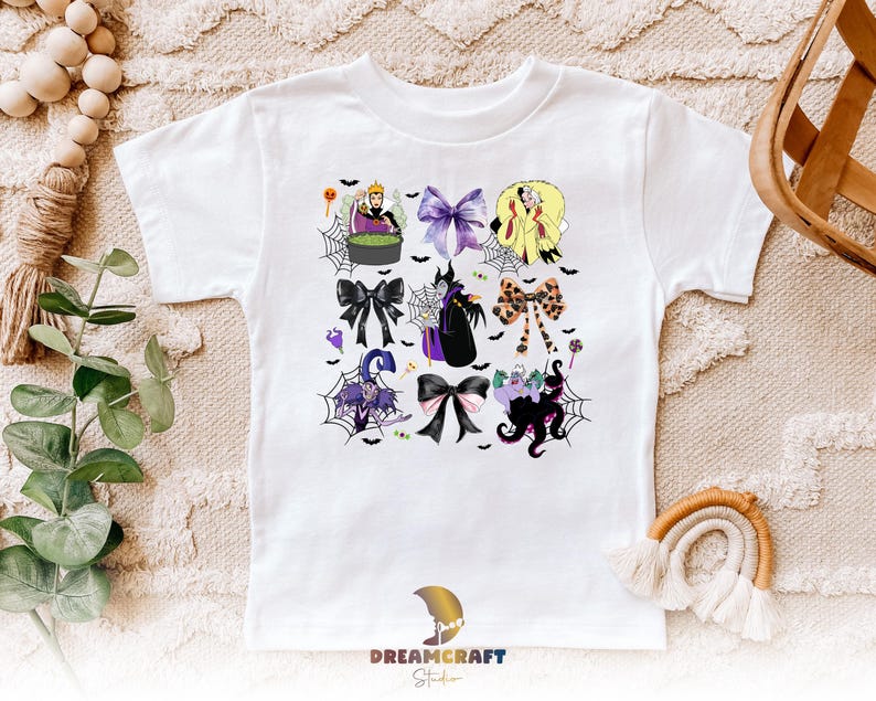 K&ouml;nnte beinhalten: Wei&szlig;es T-Shirt mit einem farbenfrohen Aufdruck von Schleifen und Halloween-Charakteren. Das Design umfasst Schurken, Spinnweben und Flederm&auml;use. Das T-Shirt hat einen Rundhalsausschnitt und kurze &Auml;rmel, f&uuml;r ein Kind.