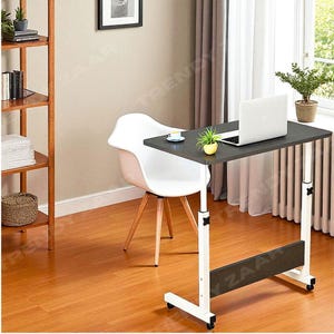 May include: An adjustable laptop desk with a dark grey top and white frame. The desk has wheels and a black support bar. A white chair with wooden legs is next to the desk. A laptop and small plant are on the desk.