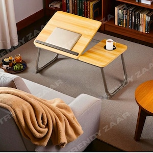 May include: A light brown wooden laptop desk with a metal frame. The desk has two sections, one for a laptop and the other with a cup holder. A laptop sits on the desk. A white mug sits in the cup holder.